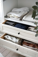 Closeup open closet drawers with folded clothes in white room minimal interior
