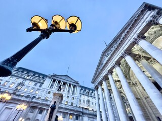 A low angle twilight view of the Bank of England and Royal Exchange buildings in the financial district of the City of London with an illuminated street lamp in the foreground. 