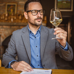 Adult man sit in a winery and hold glass of wine and clipboard