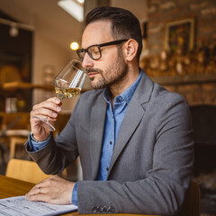 Adult man sit in a winery and hold glass of wine and clipboard
