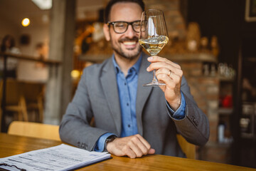Adult man sit in a winery and hold glass of wine and clipboard