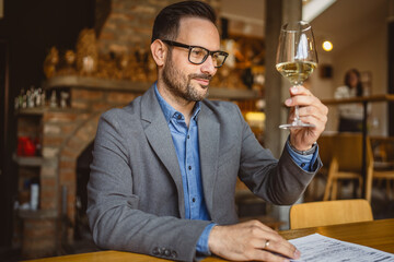 Adult man sit in a winery and hold glass of wine and clipboard