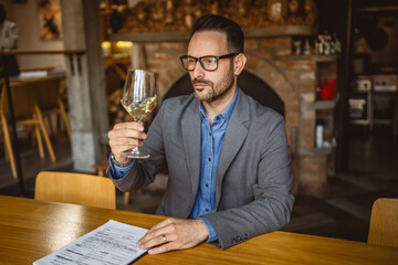 Adult man sit in a winery and hold glass of wine and clipboard