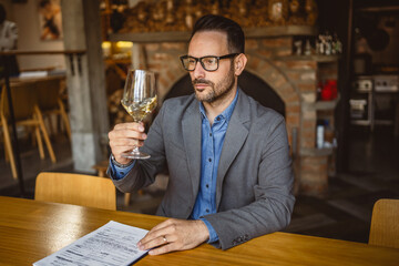 Adult man sit in a winery and hold glass of wine and clipboard