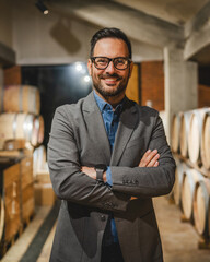 Portrait of happy adult winemaker stand between barrels in the cellar