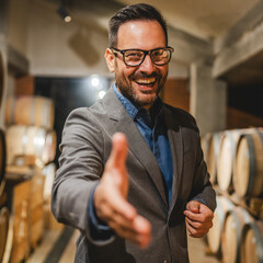 Portrait of happy adult winemaker stand between barrels in the cellar