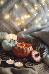 Atmospheric candle - shape of pumpkins, autumn decor on grey fall rainy day. Autumn cozy home atmosphere and inspiration, hygge concept. Aromatherapy, warming, relaxation. Wooden background