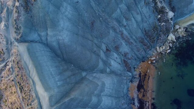 Clay cliffs flat rock cape Qarraba Bay, golden sand and emerald water in the early morning still in the shade. Aerial top down view. High quality 4k footage