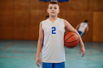 A junior basketball player is standing indoor at court with ball.