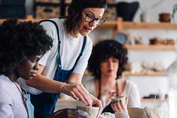 Female tutor teaching pottery her diverse attendees at ceramics studio