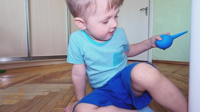 A curious boy studies an enema. Concepts of detoxification, constipation treatment, health, gastrointestinal lavage, enterosorbents, curiosity, food, pain, play, profession, medical devices, imitation