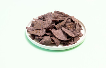Organic Blue Corn Tortilla Chips On Plate on Light Green Background. Healthy Crunchy Snack Seasoned With Sea Salt. Design Horizontal Plane.