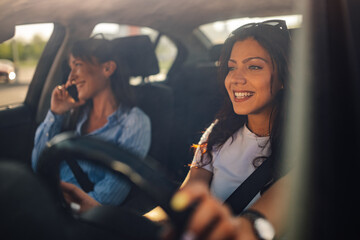 Smiling female driving a car while her friend having a phone call.