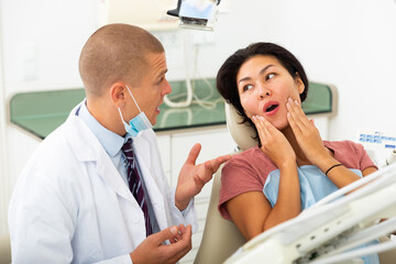 Dentist talking to asian female patient complaining of toothache at dentist office