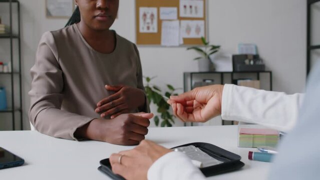 Rear view of anonymous female doctor demonstrating technique of measuring blood sugar using test strips and meter, to pregnant African American woman with diabetes during prenatal appointment