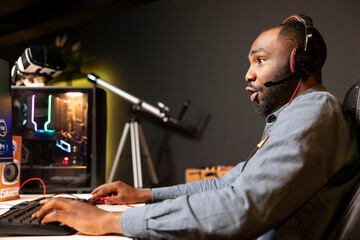 African american man wearing headphones while playing videogame at home, showing amazement emotion...