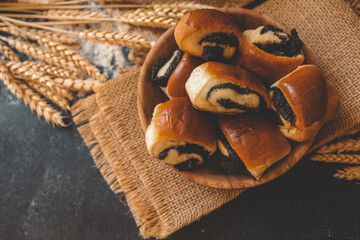 Wooden board with tasty cut poppy seed bun on table