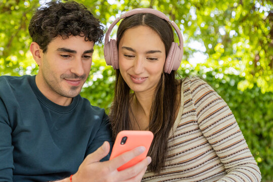 Young couple enjoying music and smartphone in park