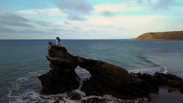 aerial shot of unrecognizable couple hugging and kissing on the edge of a rocky cliff, windy 2.7K