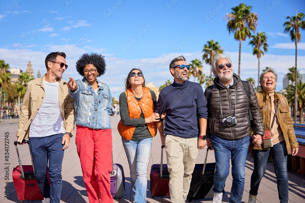 Wall mural group of cheerful middle-aged friends walking positively with their luggage along the street of a eu