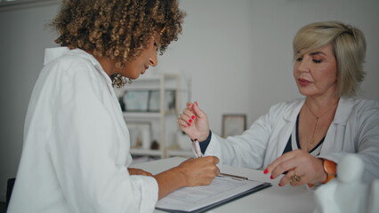 Woman signing medical form in modern clinic closeup. Friendly nurse talking