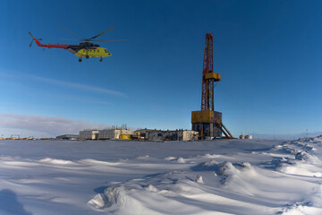 Drilling derrick and well drilling infrastructure in the northern oil and gas field. Polar snowy winter. Yellow helicopter carrying drillers. Clear blue sky. Collage