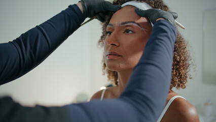 Cosmetologist shaping woman brows in beauty salon closeup. Curly girl visiting