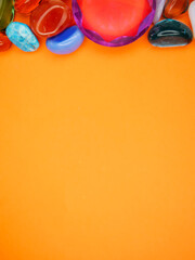 A colorful assortment of gemstones and crystals are arranged on a bright orange background. The...