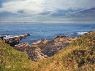 The ocean is calm and the sky is blue. The water is clear and the rocks are brown. Rough stone coast of Ireland. Mullaghmore area. Loved by tourist shore with stunning Irish nature scenery.