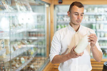 Man in bio supermarket buys daily product milk. Male buyer examines packaging of product and reads...