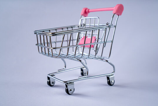 A small shopping cart with a pink handle on a gray background - Powered by Adobe