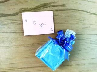 Blue gift box, paper note written I love you on the wooden blackground.
