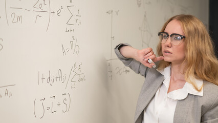 Young woman scientist writes formulas on a white board.