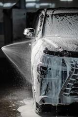 Man applying foam to black car in car wash. Vertical photo. 