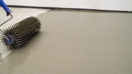A craftsman's hand with a needle roller for a new concrete screed with self-leveling cement mortar...