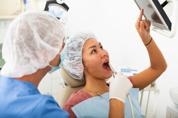 Dentist in face mask scanning the teeth of female patient during checkup at dental clinic office