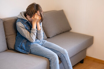 sad boy sits on couch covering face, abuse and deep emotional distress, Mental health crisis,...