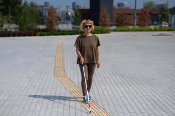 An elderly blind woman walks with a cane along a tactile tile. 