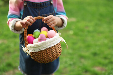 Easter celebration. Little girl holding basket with painted eggs outdoors, closeup. Space for text