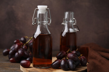 Bottles with wine vinegar and grapes on wooden table, closeup