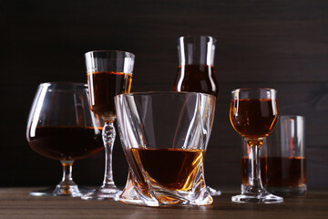 Different delicious liqueurs in glasses on wooden table