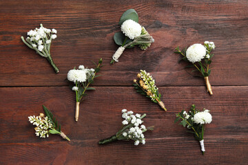 Small stylish boutonnieres on wooden table, flat lay