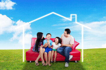 Happy family sitting on red sofa outdoor with house picture