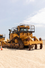 Yellow Crawler Dozer On Sandy Beach, Blue Sky On Background. Bulldozer Builds Roads. Construction And Landfill Equipment And Machinery. No People. Vertical Plane