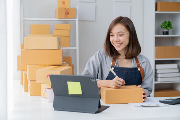 Delivery business. happy modern female checking order with laptop and using smartphone applications in the warehouse