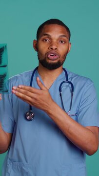Vertical video Healthcare professional informing patient of radiology x ray scan results, studio backdrop. African american doctor presenting radiography and providing injury treatment, camera B