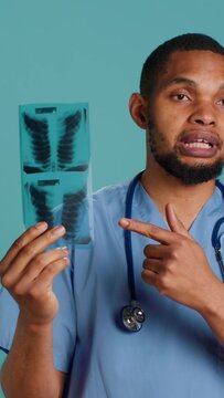Vertical video Healthcare professional informing patient of radiology x ray scan results, studio backdrop. African american doctor presenting radiography and providing injury treatment, camera A