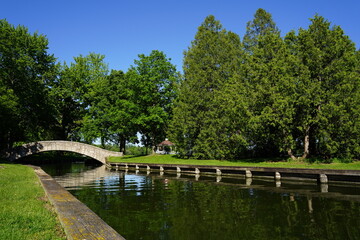 Stone walking bridge arches over a river through a community park.