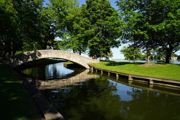 Stone walking bridge arches over a river through a community park.