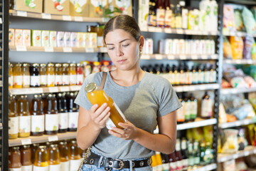 In bio ecological goods store, girl buyer carefully examines and view product, bottle of juice....